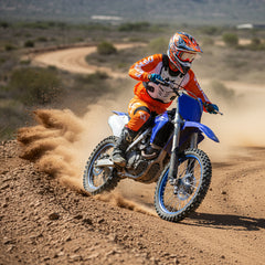 Motocross rider in orange gear drifting a blue dirt bike on a dusty desert trail.