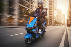Person riding a blue scooter with orange accents on a city street.
