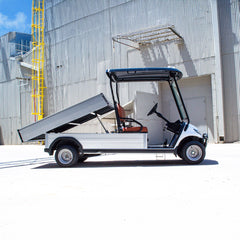 Golf cart with an open cargo bed in front of a large industrial building.