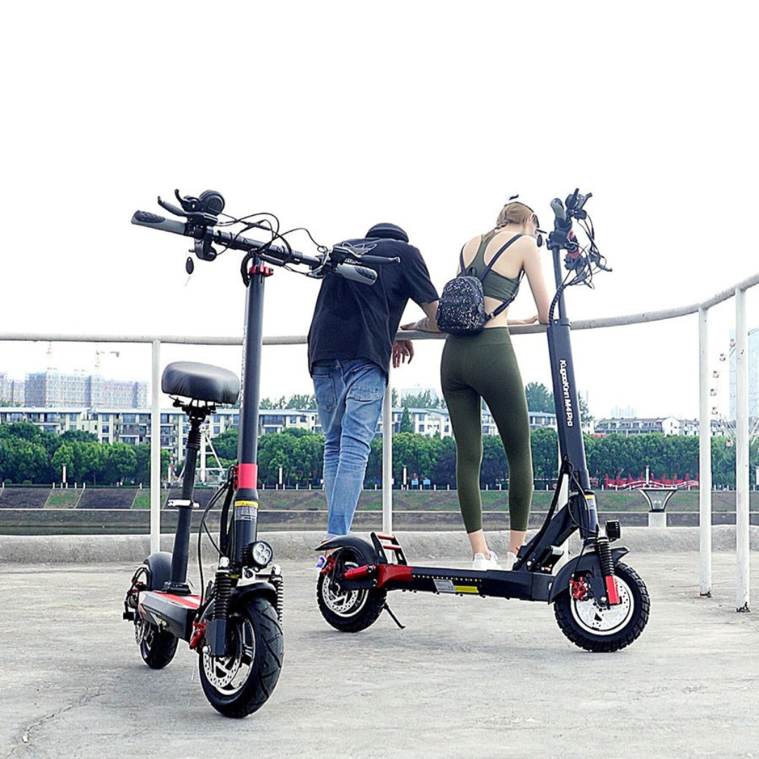 Two people standing next to electric scooters on a bridge