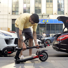 Man adjusting an electric scooter on a city street with cars